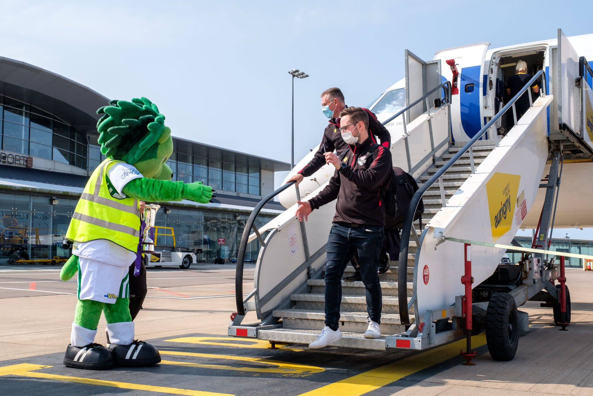 Guernsey's club mascot greets FC Isle of Man players at Guernsey Airport.
